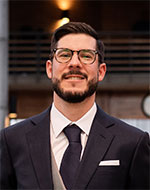 Nicolás Pablo Rodríguez Rioseco. He is wearing a navy blue suit jacket, matching tie and white shirt. He has a short beard, and wears glasses.