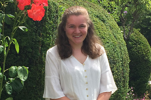 Lauren Holmes standing in front of a hedge with a pink flower to the left of her