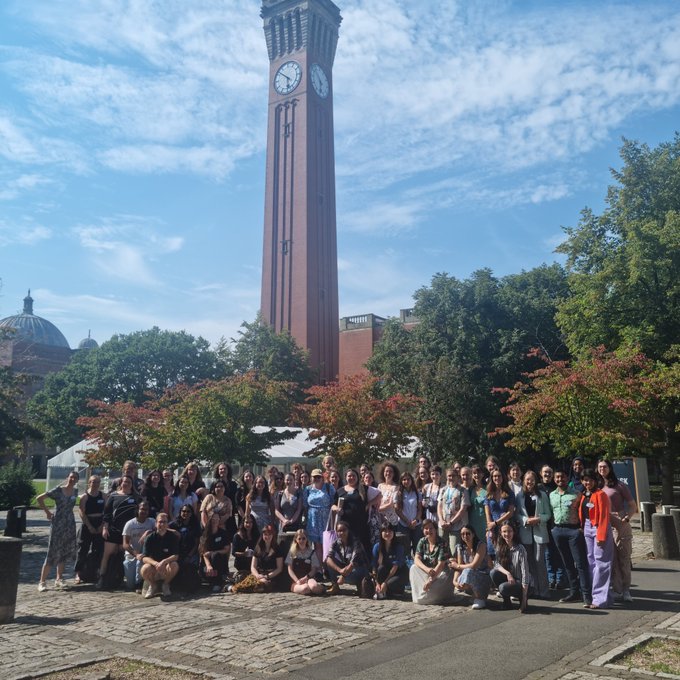 A group of students gathered in a green space in front of trees