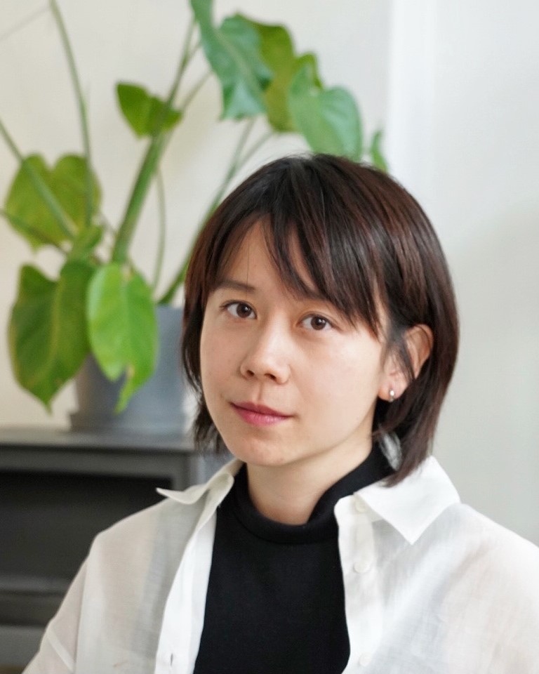 A photo of Yunyun against a plain background, with a plant visible in the background