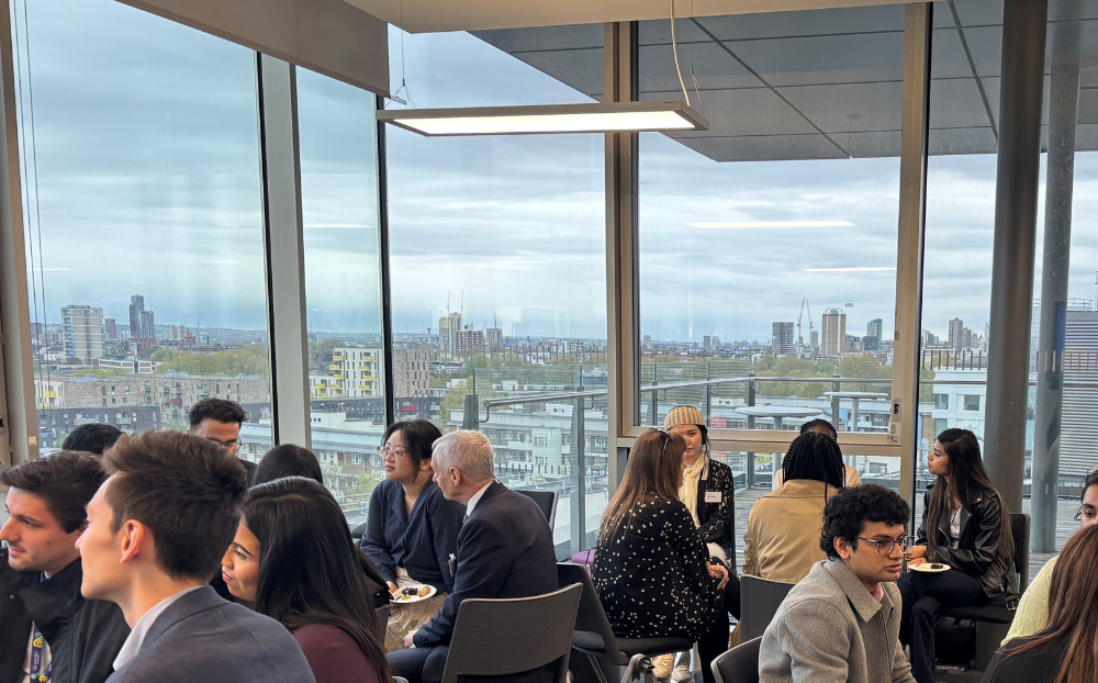 People sitting in groups speaking in a room with a view of the london skyline