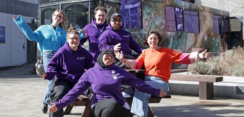 Student ambassadors, outreach officer, and artist sat on a bench next to moon palace bus