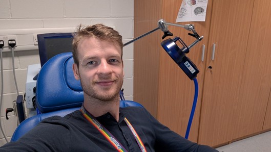 Gwijde Maegherman sitting in a chair behind a microphone. Looking at the camera in a grey top with a lanyard.