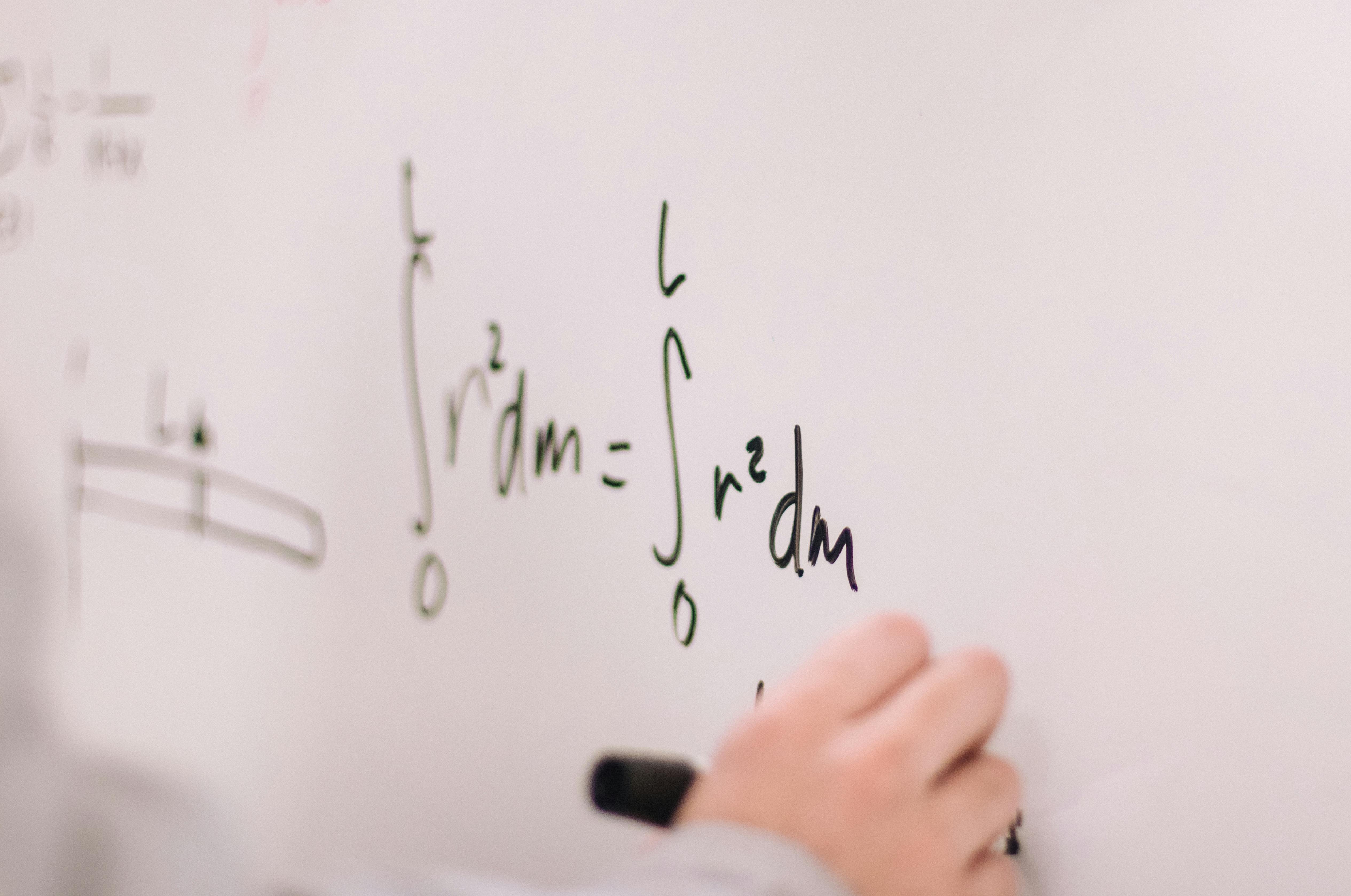 a teacher writing mathematical equations on a whiteboard