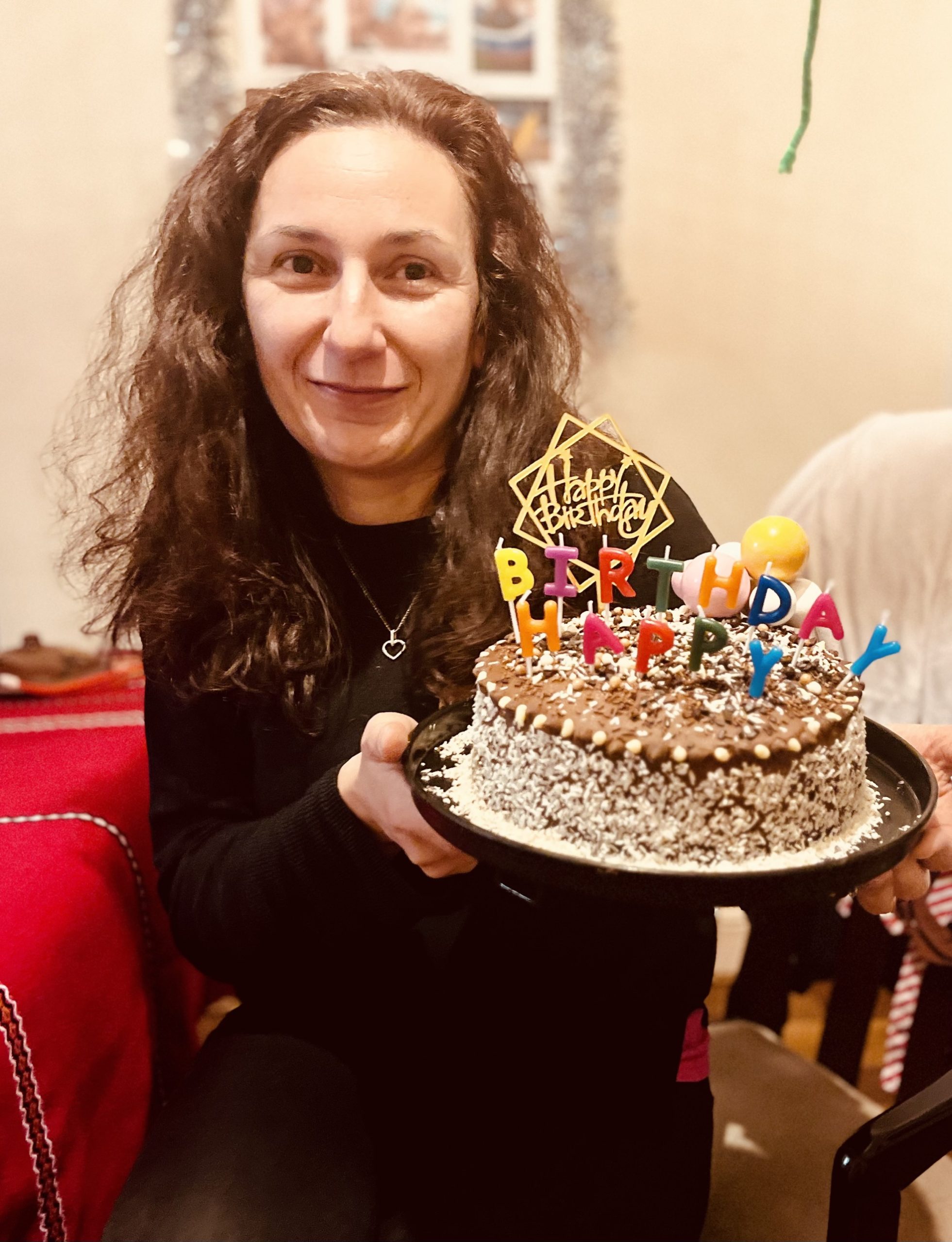 Yanna looking at the camera holding a cake with candles. She is wearing a black top.